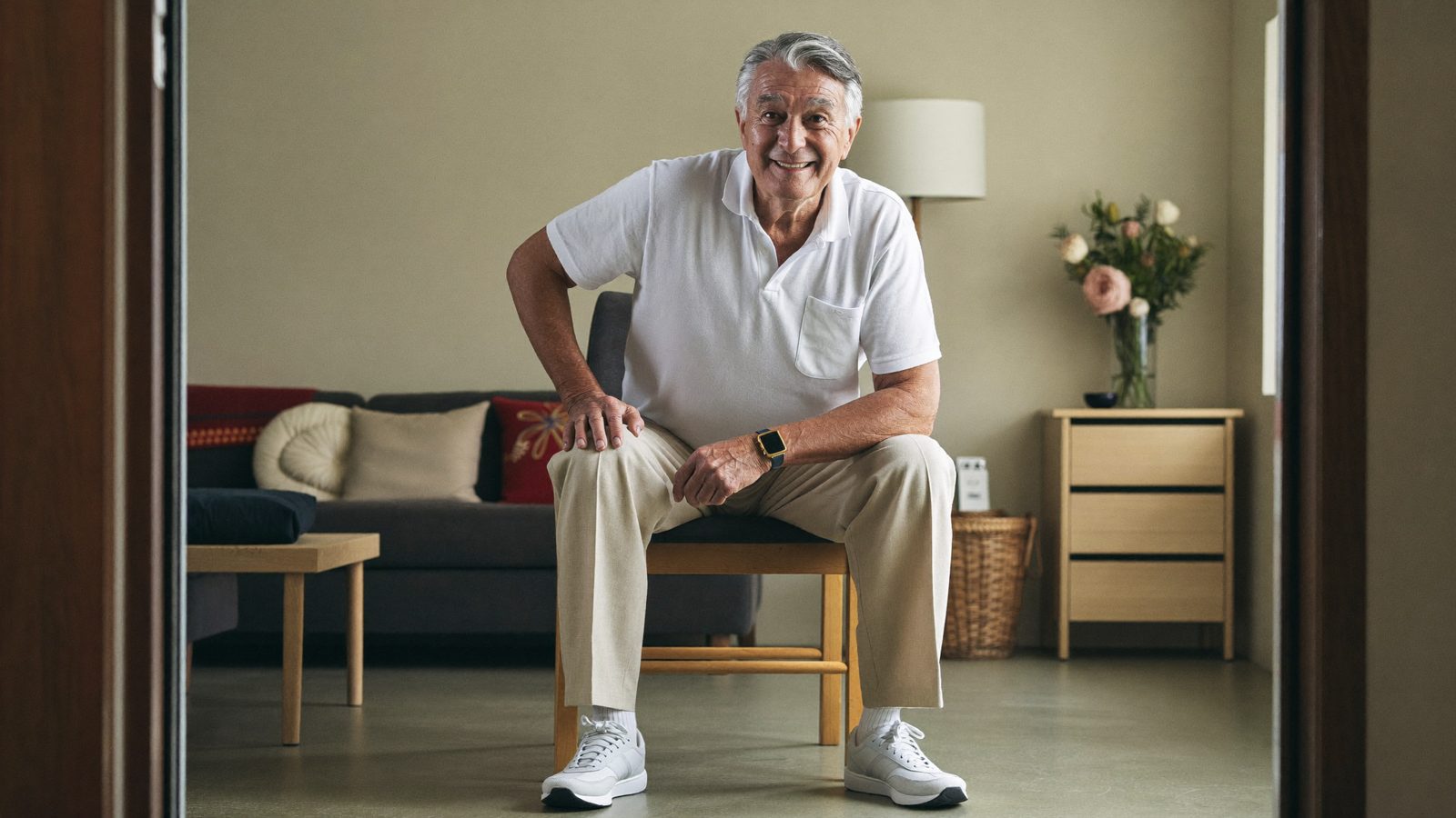 Senior man practicing a gentle balance exercise at home with one hand on a sturdy chair