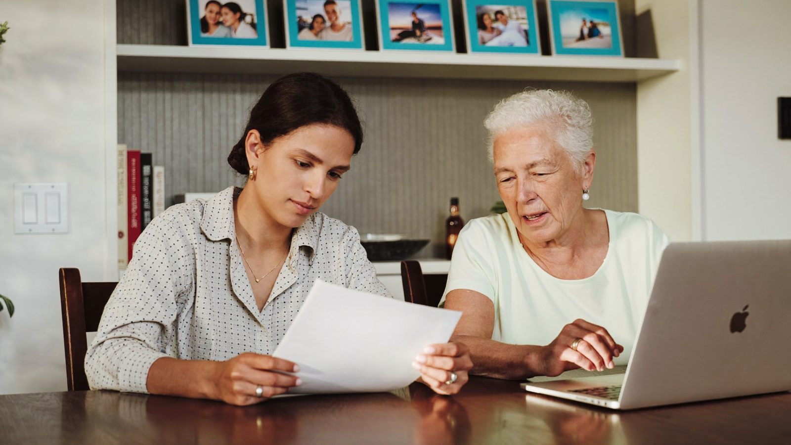 Adult daughter sitting at a kitchen table with her mother, reviewing paperwork together over coffee
